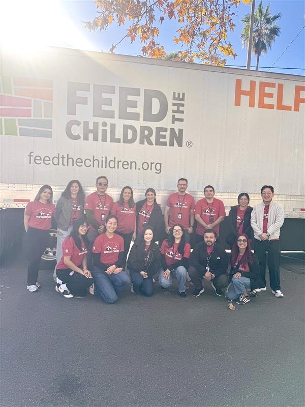 Group of Panda Cares volunteers in matching red shirts pose together in front of a Feed the Children truck during a community food distribution event